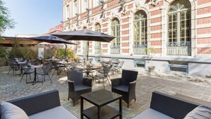 An outdoor patio with wicker furniture and umbrellas, set against a historic building with large windows and decorative elements. - Best Western Urban Hotel  (Lille)