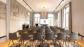 A conference room with rows of chairs, a large screen, and a patterned carpet.