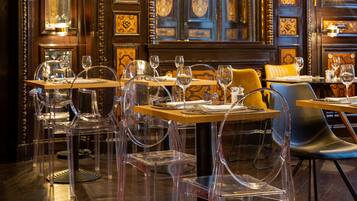 A restaurant interior with clear glass chairs, wooden tables, and ornate wall decorations.