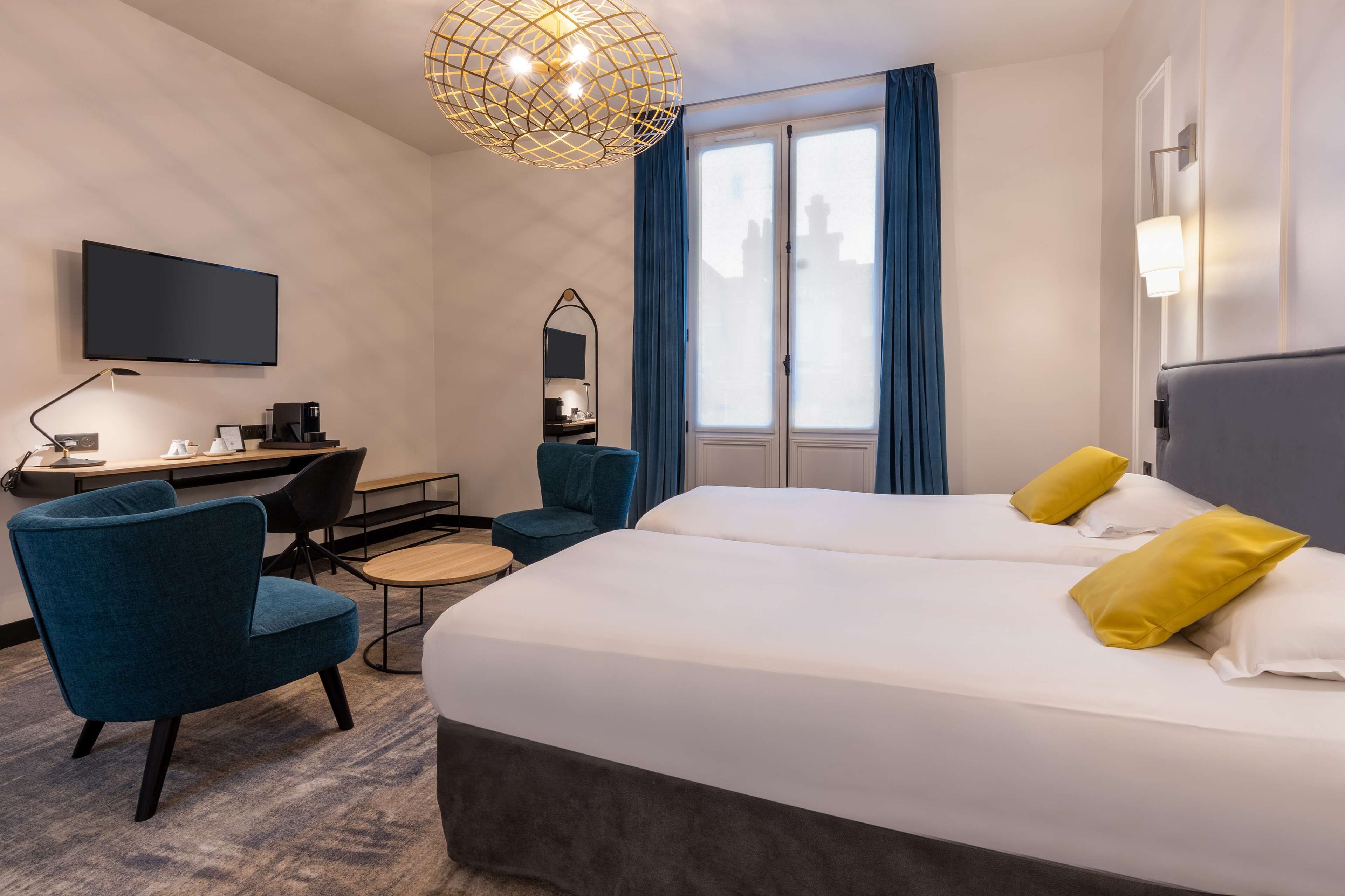 Une chambre d’hôtel avec un grand lit, un bureau avec une chaise, une télévision et une grande fenêtre avec des rideaux.