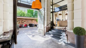 A spacious lobby with a staircase, a seating area with a red sofa, and a large window overlooking greenery. - Best Western Urban Hotel  (Lille)