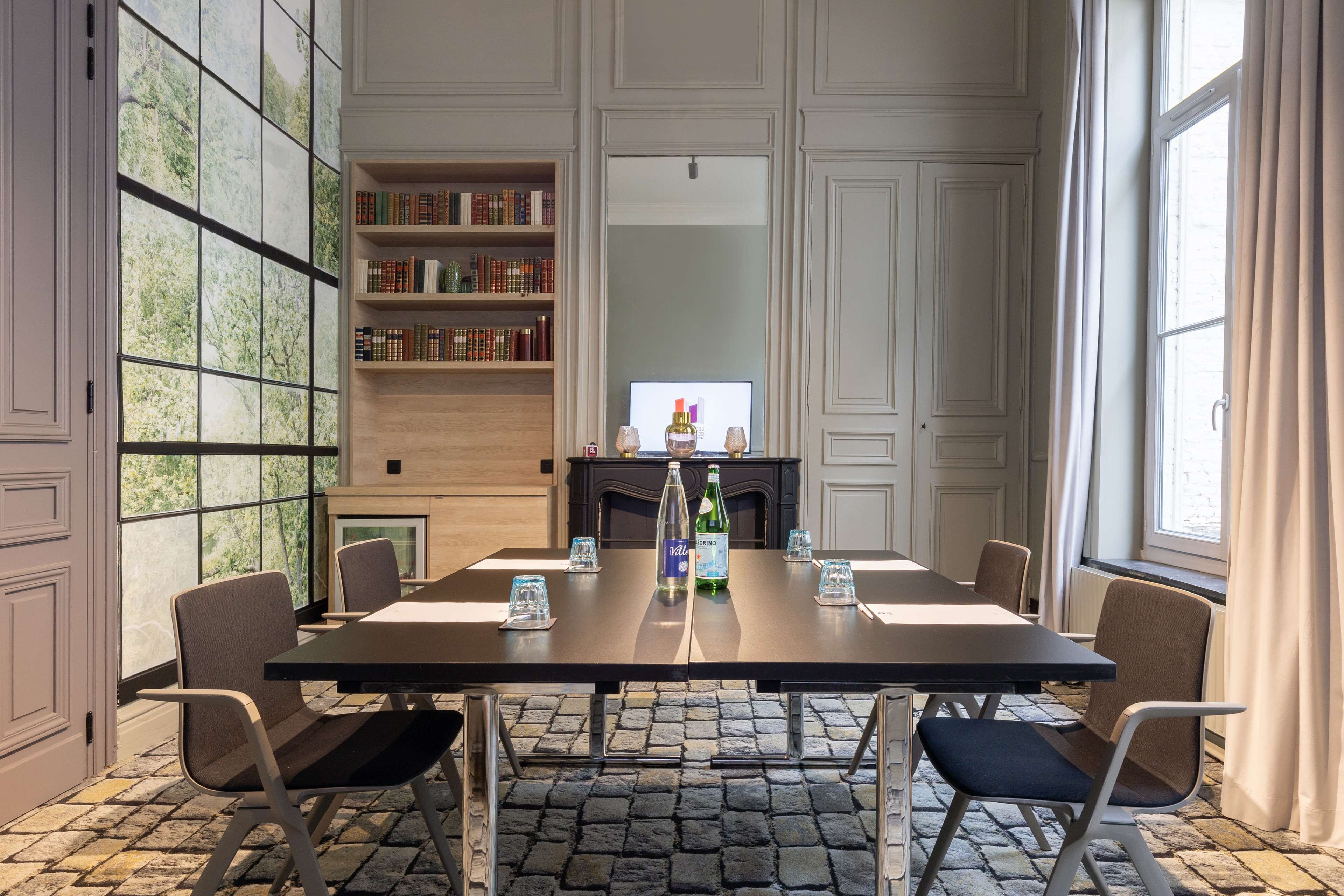 A conference room with a long table, chairs, a bookshelf, a fireplace, and a large window with curtains.