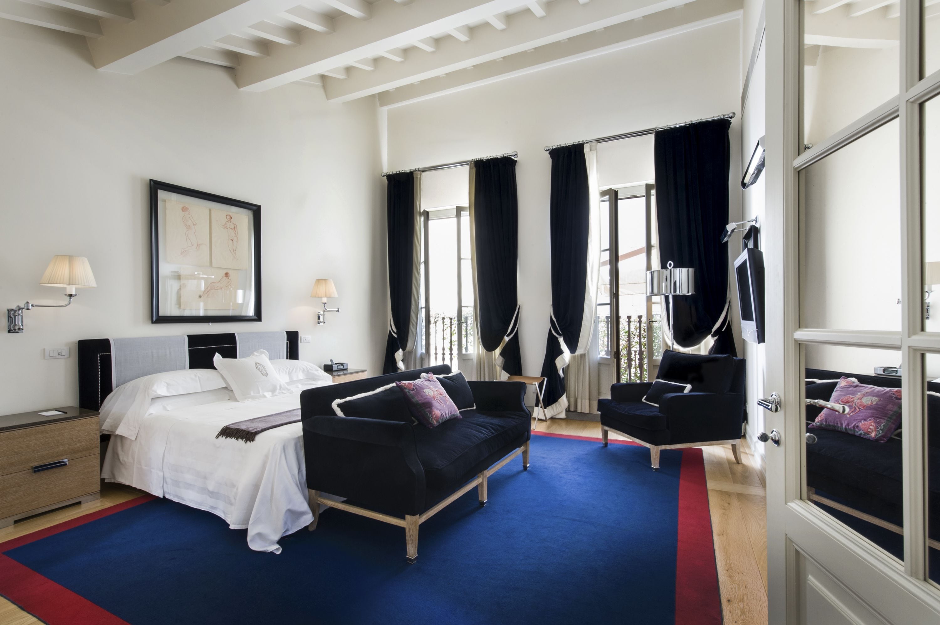Une chambre d’hôtel avec un lit, un canapé noir, une petite table, une chaise et une fenêtre avec des rideaux.