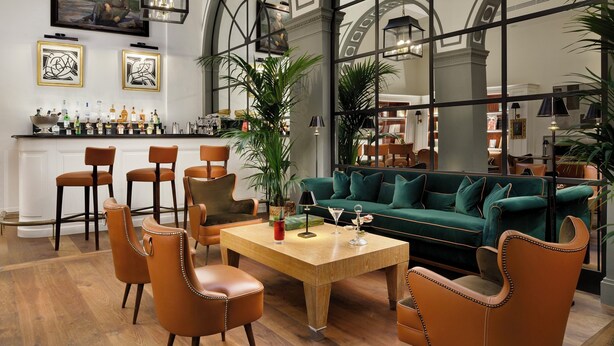 A spacious living area with a green sofa, leather chairs, a wooden coffee table, and a bar with bottles. - Palazzo Vecchietti (Florence)