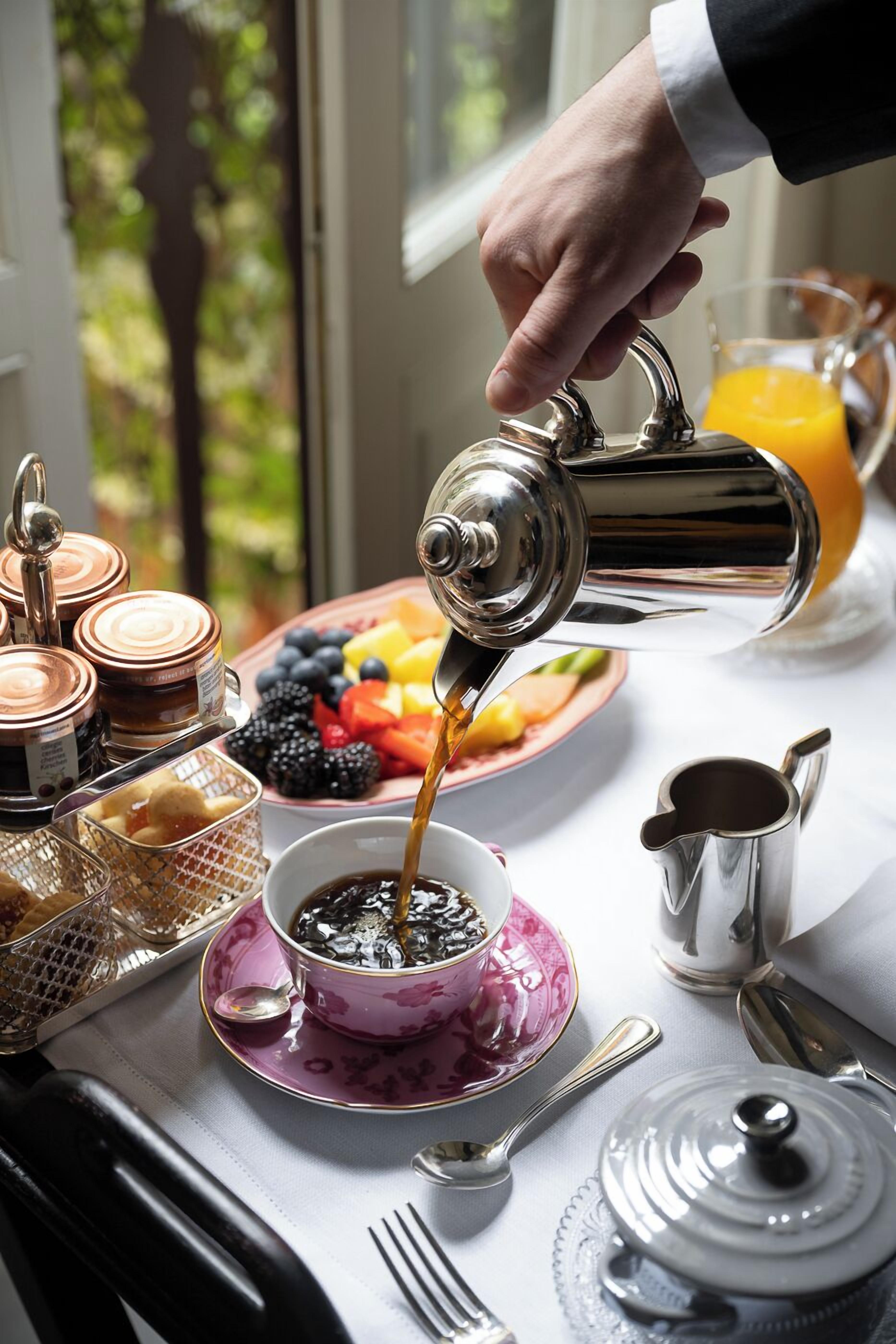 A breakfast setting with a coffee pot pouring into a cup, a fruit bowl, and various breakfast items on a table.