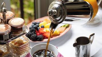 A breakfast setting with a coffee pot pouring into a cup, a fruit bowl, and various breakfast items on a table.