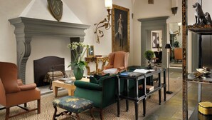 A room with a fireplace, a green armchair, a brown leather chair, a wooden table, and a large mirror. - Palazzo Vecchietti (Florence)