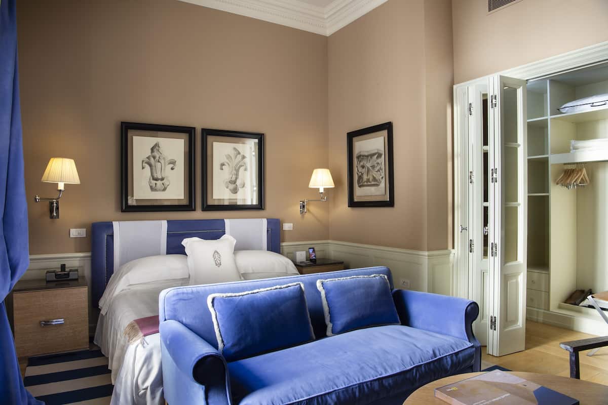 A hotel room with a bed, a blue sofa, a wardrobe, and two wall-mounted lamps.