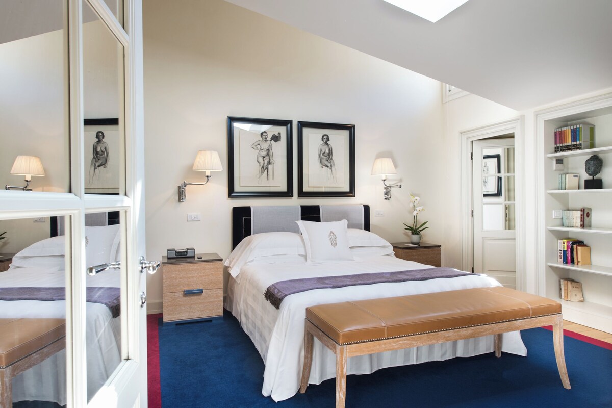 A neatly arranged bedroom with a large bed, bedside tables, a bench, and a bookshelf.