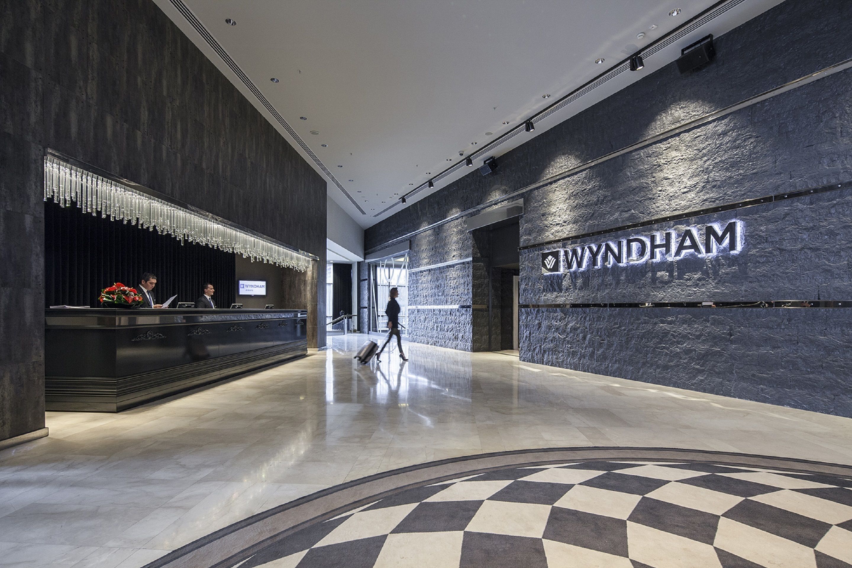 Un vestíbulo moderno con un mostrador de recepción, un gran letrero 'WYNDHAM' y un piso con diseño de cuadros.