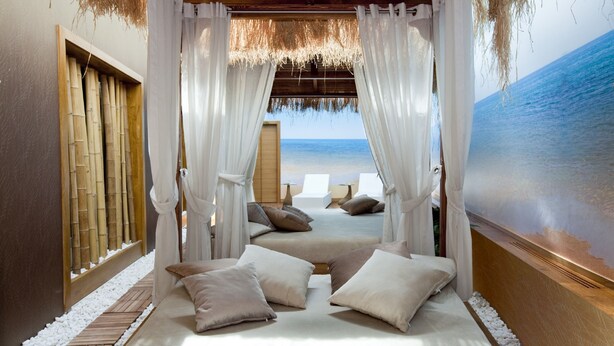 Una habitación frente a la playa con una cama, cortinas blancas y vista al océano.
