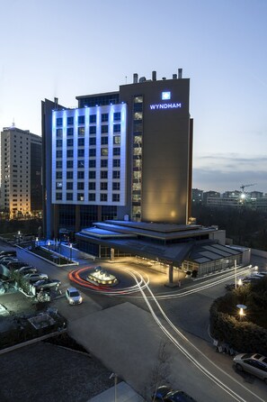 A modern hotel with a prominent 'WYNDHAM' sign, featuring a central atrium and a parking area with light trails from moving vehicles. - Wyndham Ankara (Ankara)