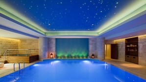 Una amplia piscina interior con techo estrellado, caída de agua y zona de terraza de madera.