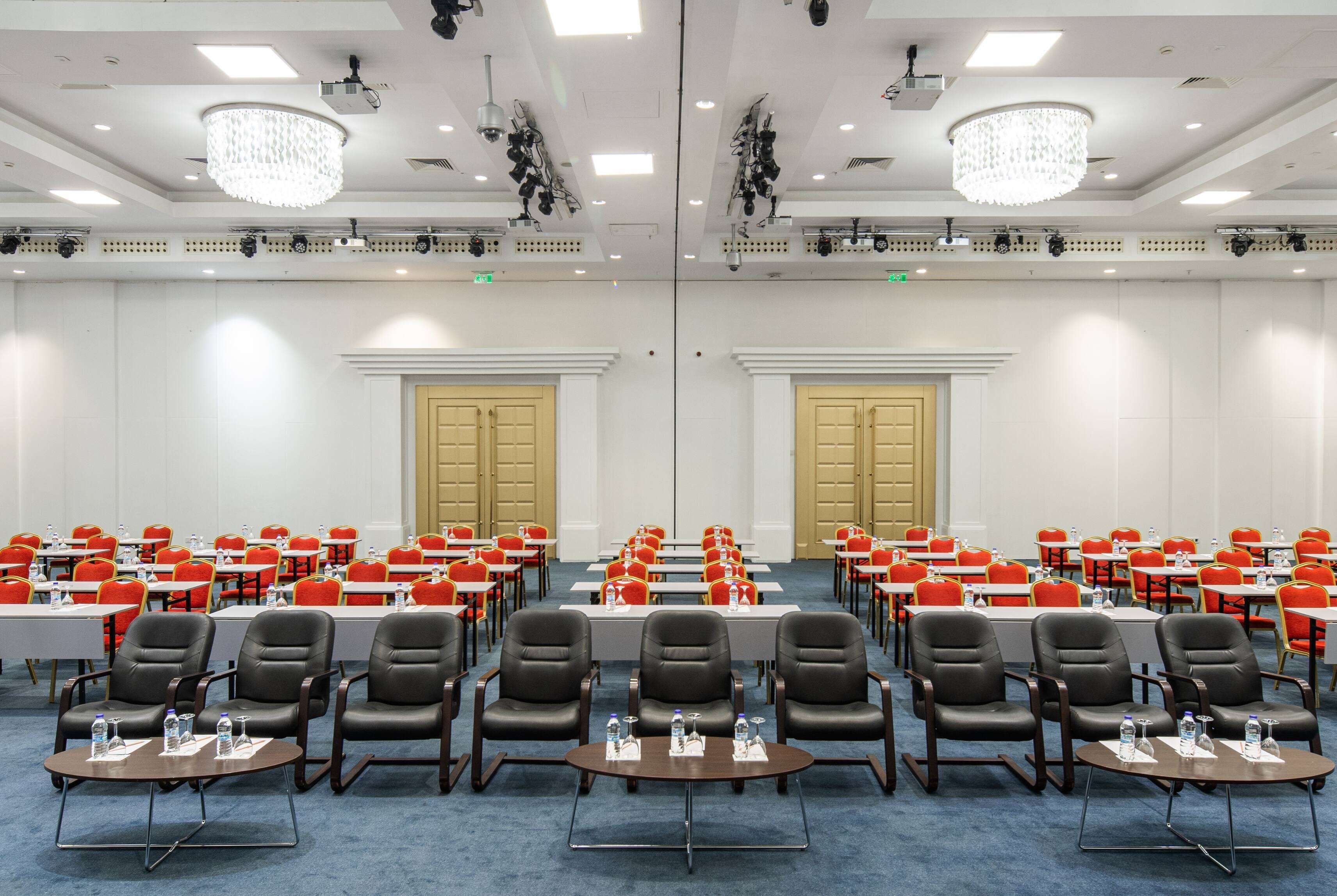 A conference room with rows of tables and chairs, equipped with water bottles, and a chandelier on the ceiling.