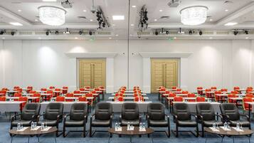 A conference room with rows of tables and chairs, equipped with water bottles, and a chandelier on the ceiling.