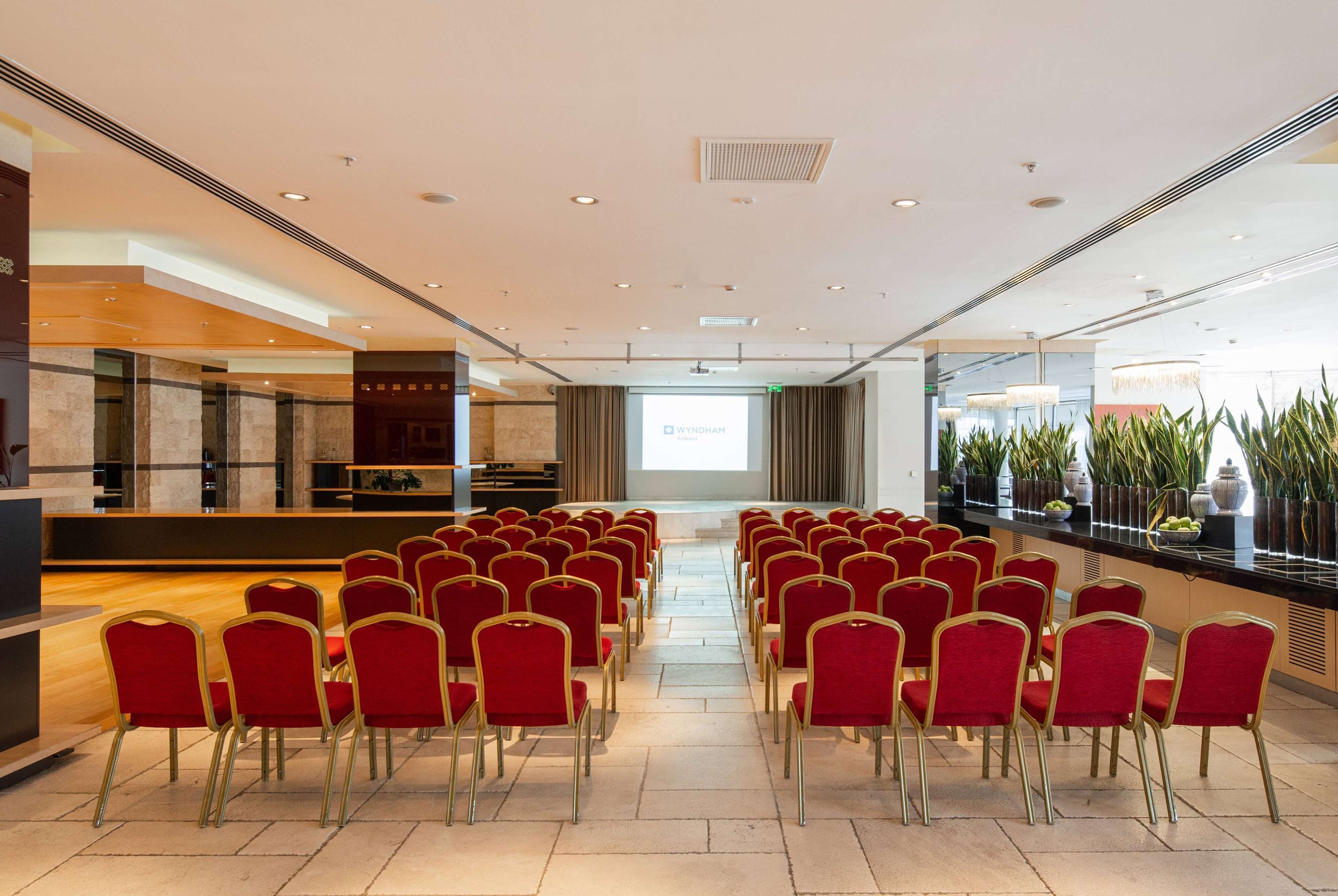 A conference room with rows of red chairs facing a projection screen displaying "WYNDHAM."