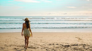 A person walking on a sandy beach with waves in the background. - Away Bali Legian Camakila Resort (Legian)