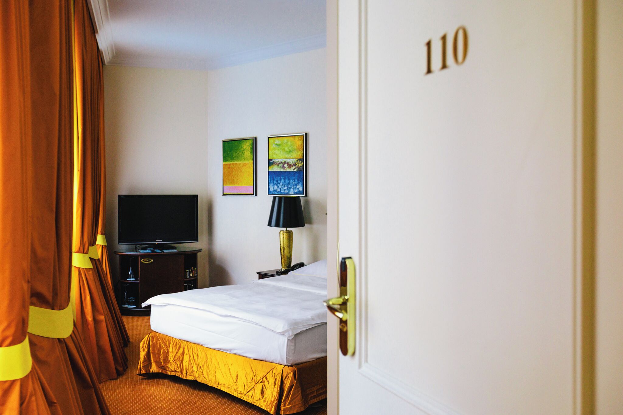 Ein Hotelzimmer mit einem Bett, einem Fernseher, einer Lampe und zwei Bildern an der Wand.
