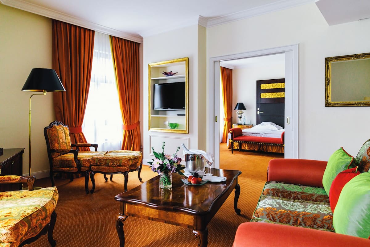 Una habitación de hotel con una mesa de centro de madera, un sofá, un televisor en la pared y una cama con cabecera a rayas.