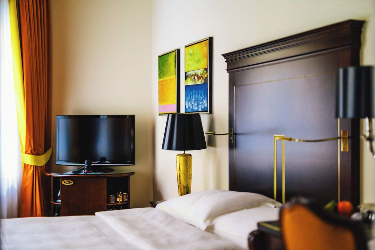 Una habitación de hotel con cama, televisión, lámpara y obras de arte en la pared.