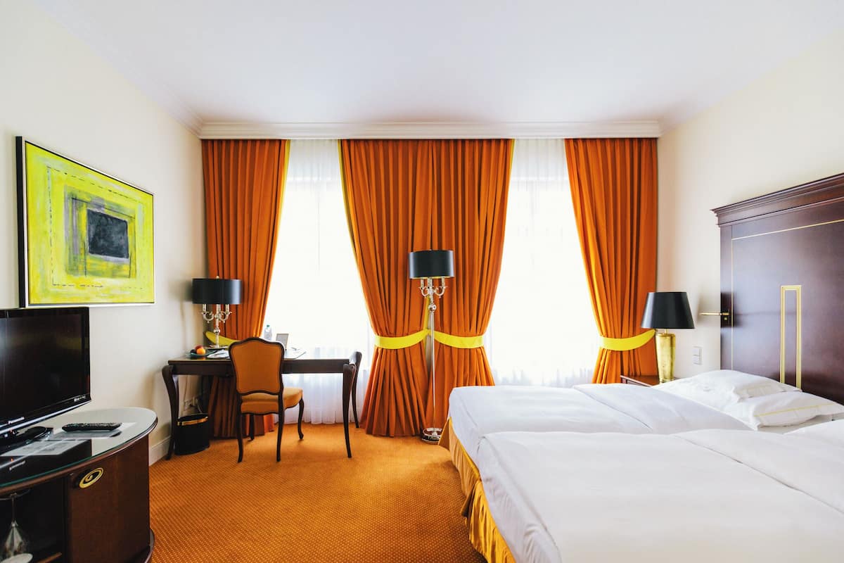 Habitación de hotel con cama, escritorio, silla, televisor y cortinas.