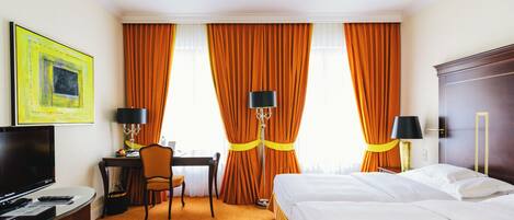 A hotel room with a bed, desk, chair, television, and curtains.