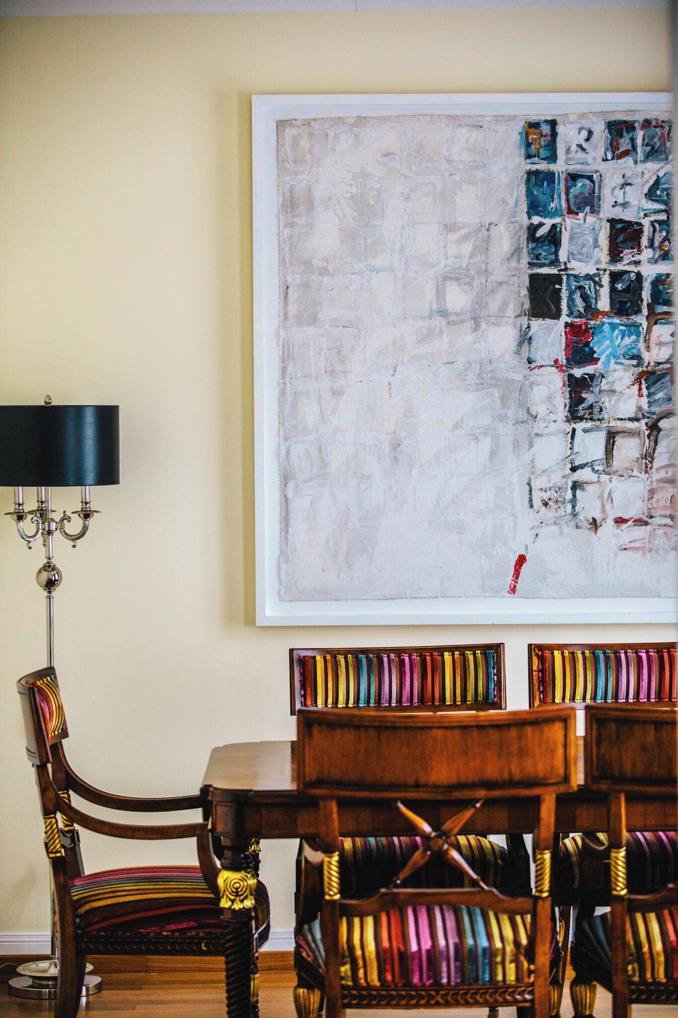 A dining area with a table and chairs, a wall-mounted painting, and a floor lamp.