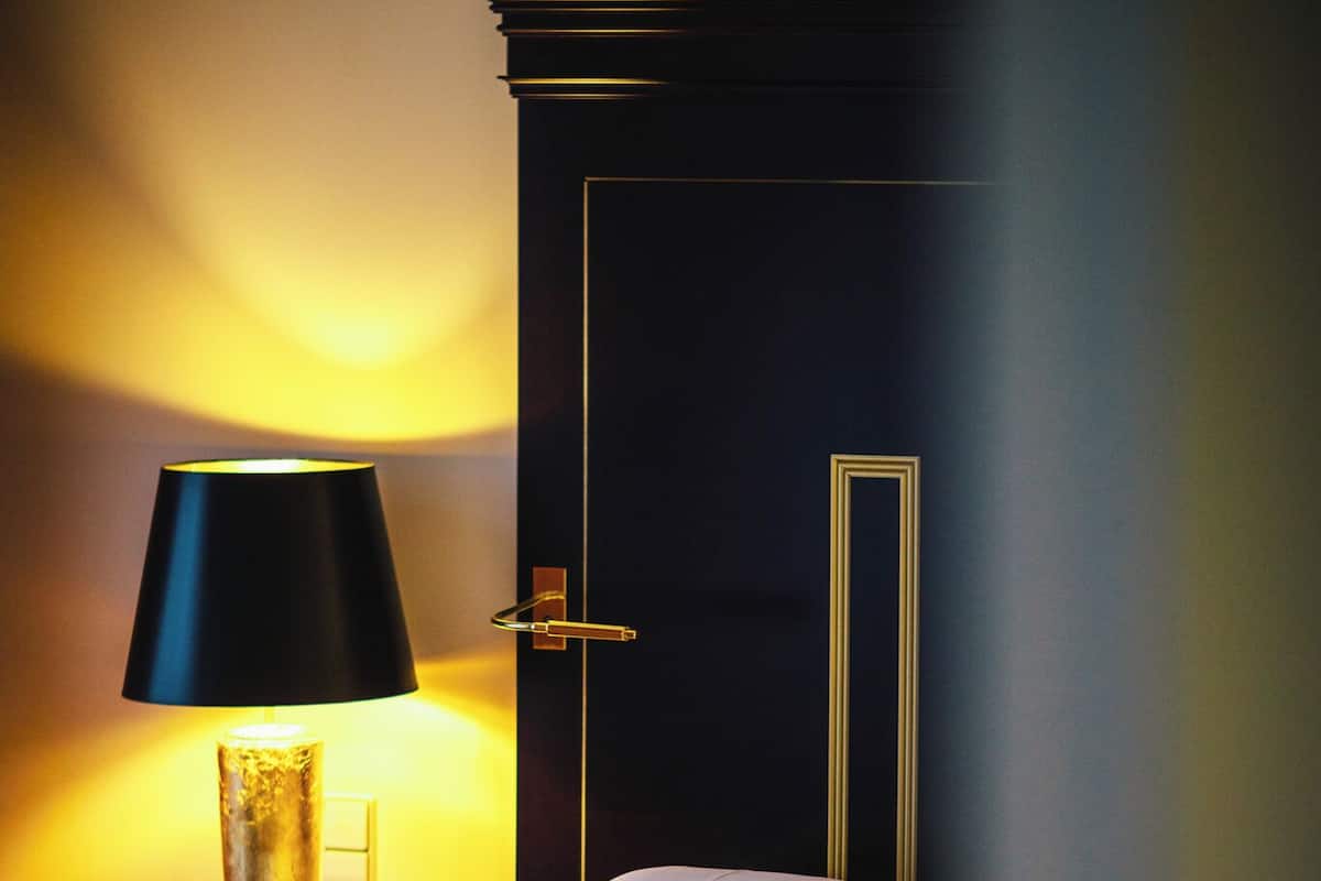 Una habitación de hotel con una cama, una mesita de noche, una lámpara y una puerta.