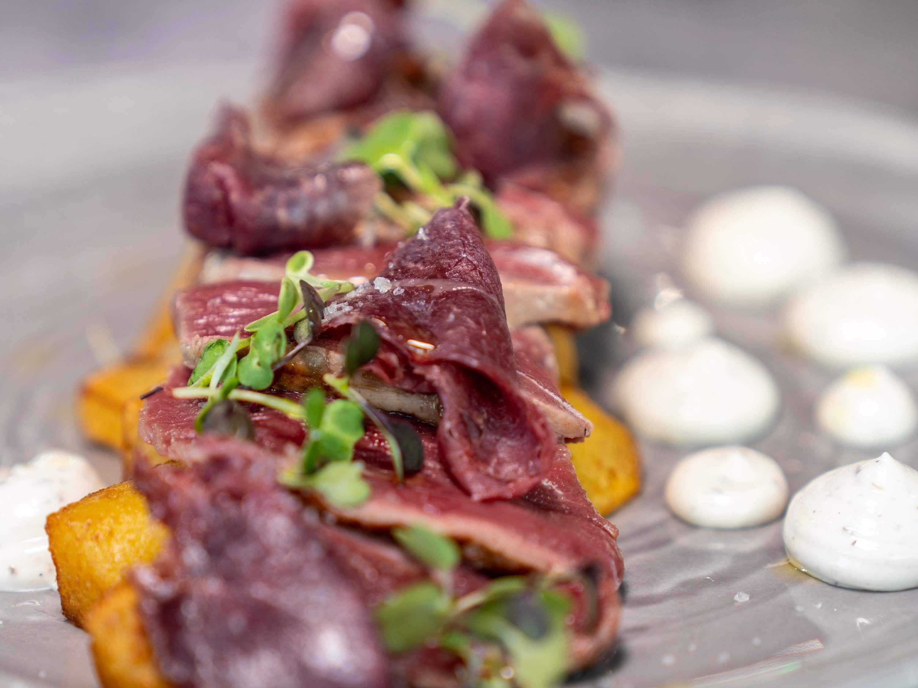 A dish with meat, greens, and a creamy sauce on a plate.