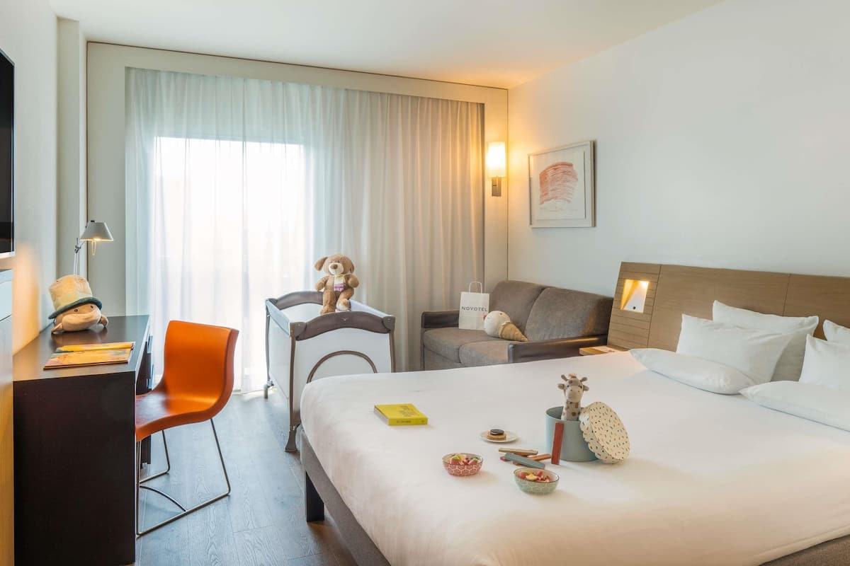 A hotel room with a bed, a desk, a chair, a sofa, and a window with curtains.