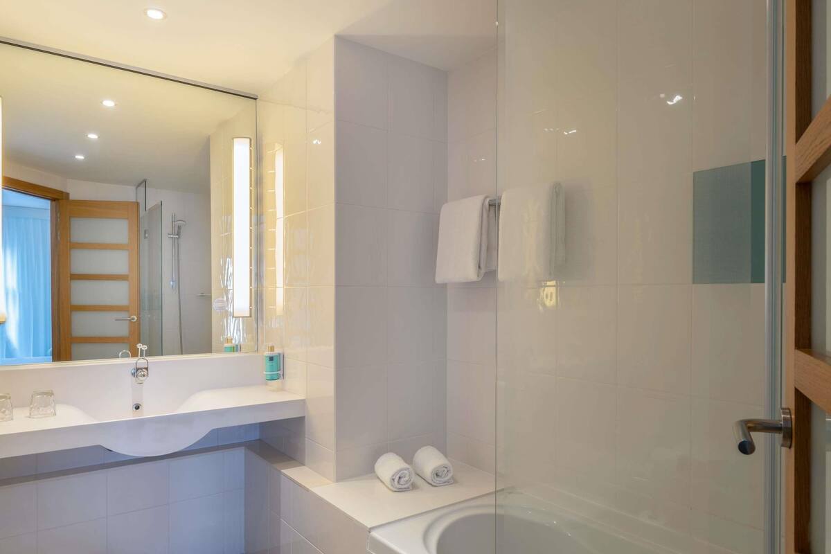 A modern bathroom with a glass-enclosed shower, a large mirror, and a white sink.