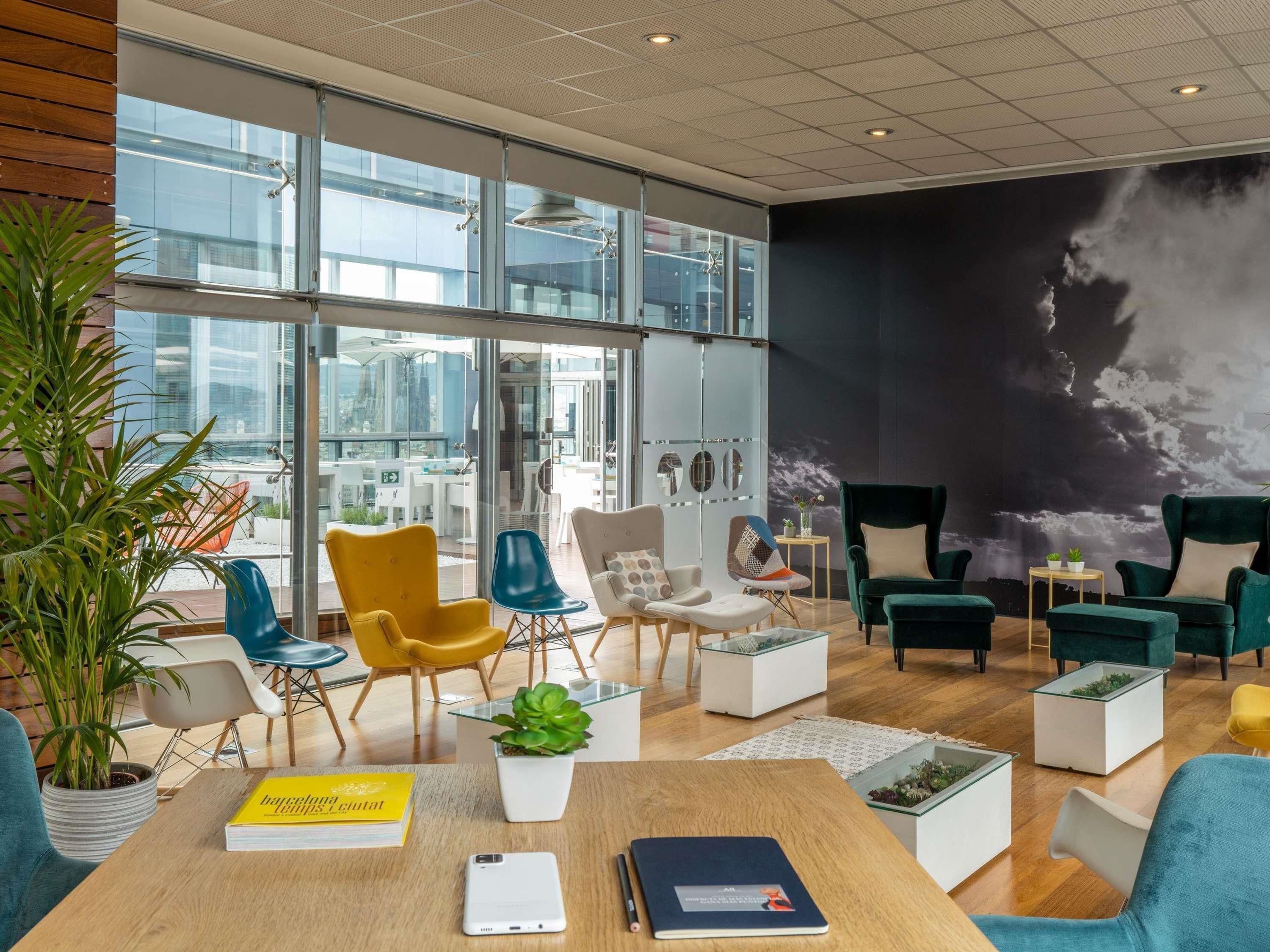 Een moderne lounge met een hoge plafond, grote ramen en een muurschildering.