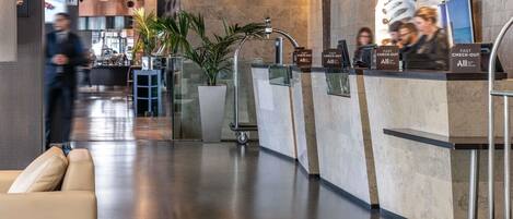Un vestíbulo moderno de hotel con recepción, zona de estar y vistas al bar.
