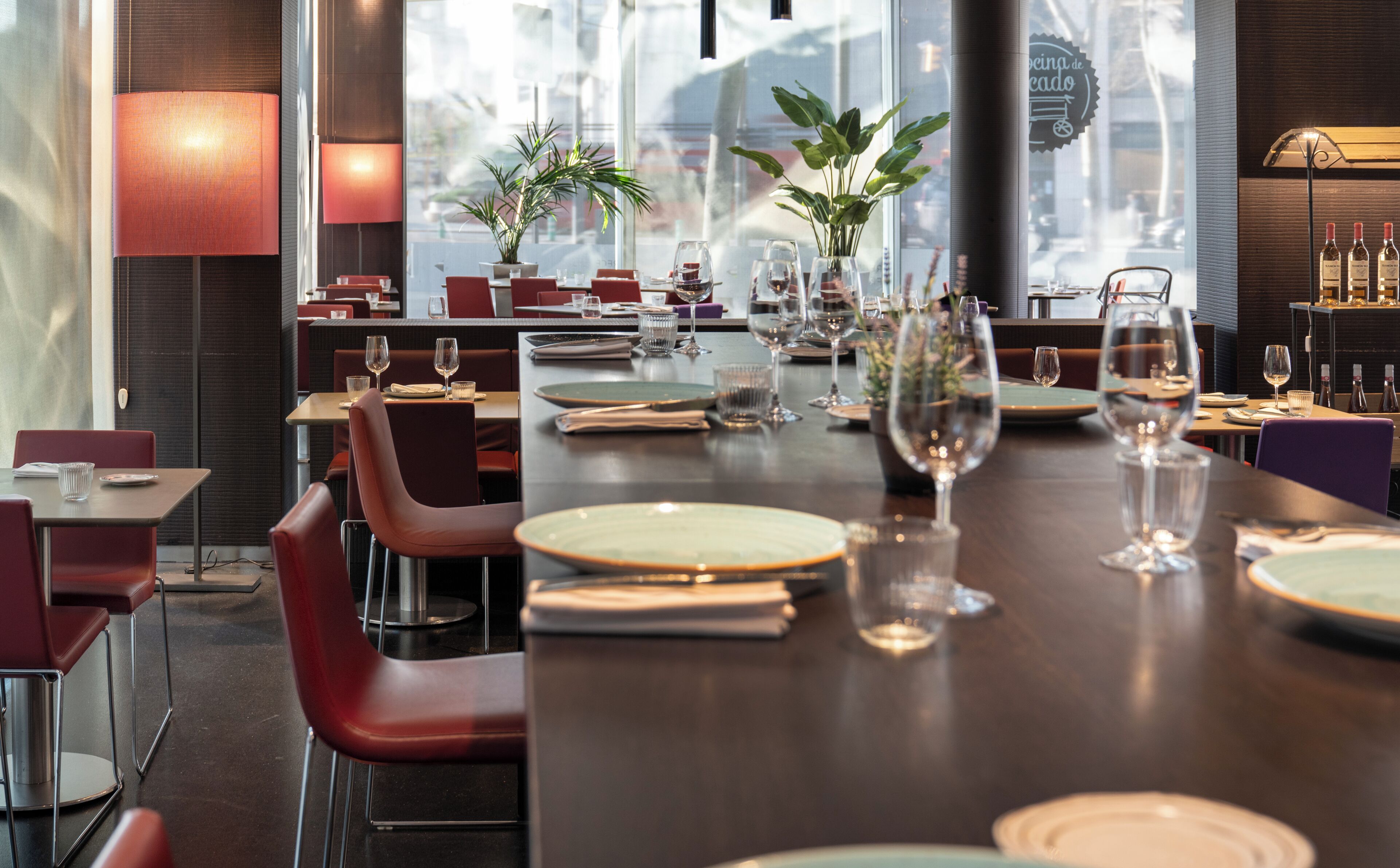 A restaurant with tables set for dining, featuring a modern interior with red chairs and a large window offering a view of the city.