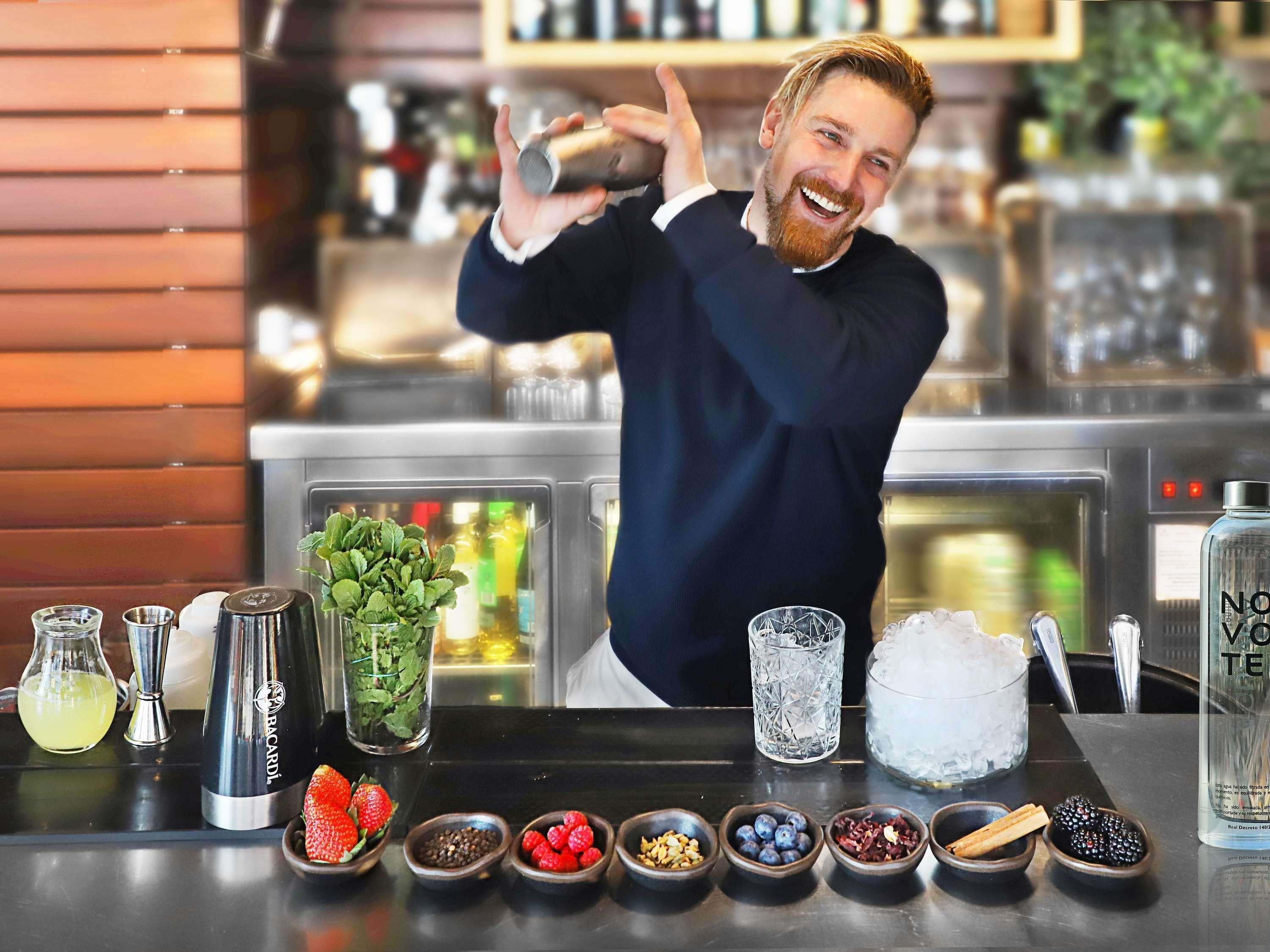 A bartender preparing a drink with various ingredients and tools on a bar counter.