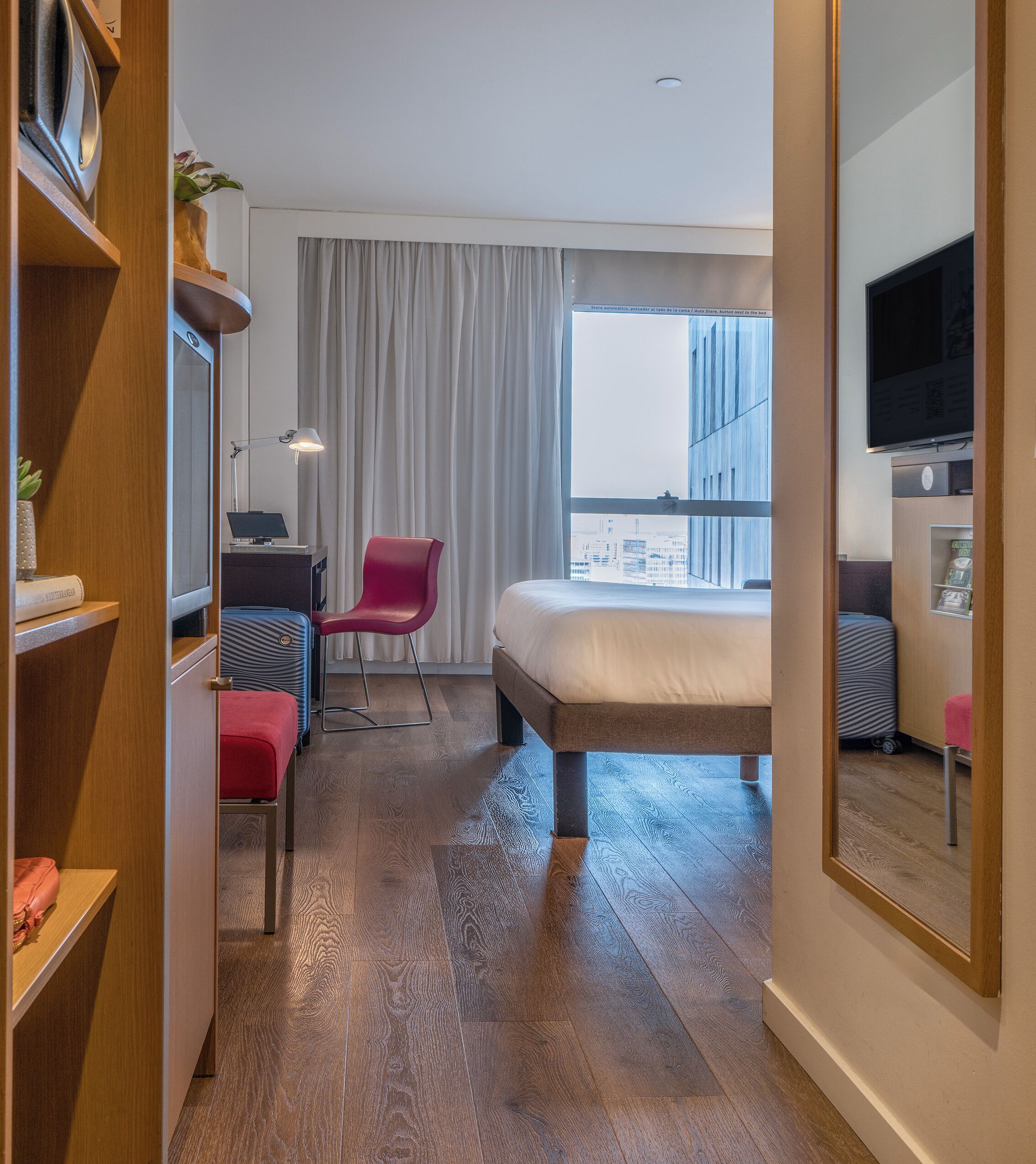 Ein Hotelzimmer mit Bett, Schreibtisch, Stuhl, Fernseher und einem Fenster mit Vorhängen.