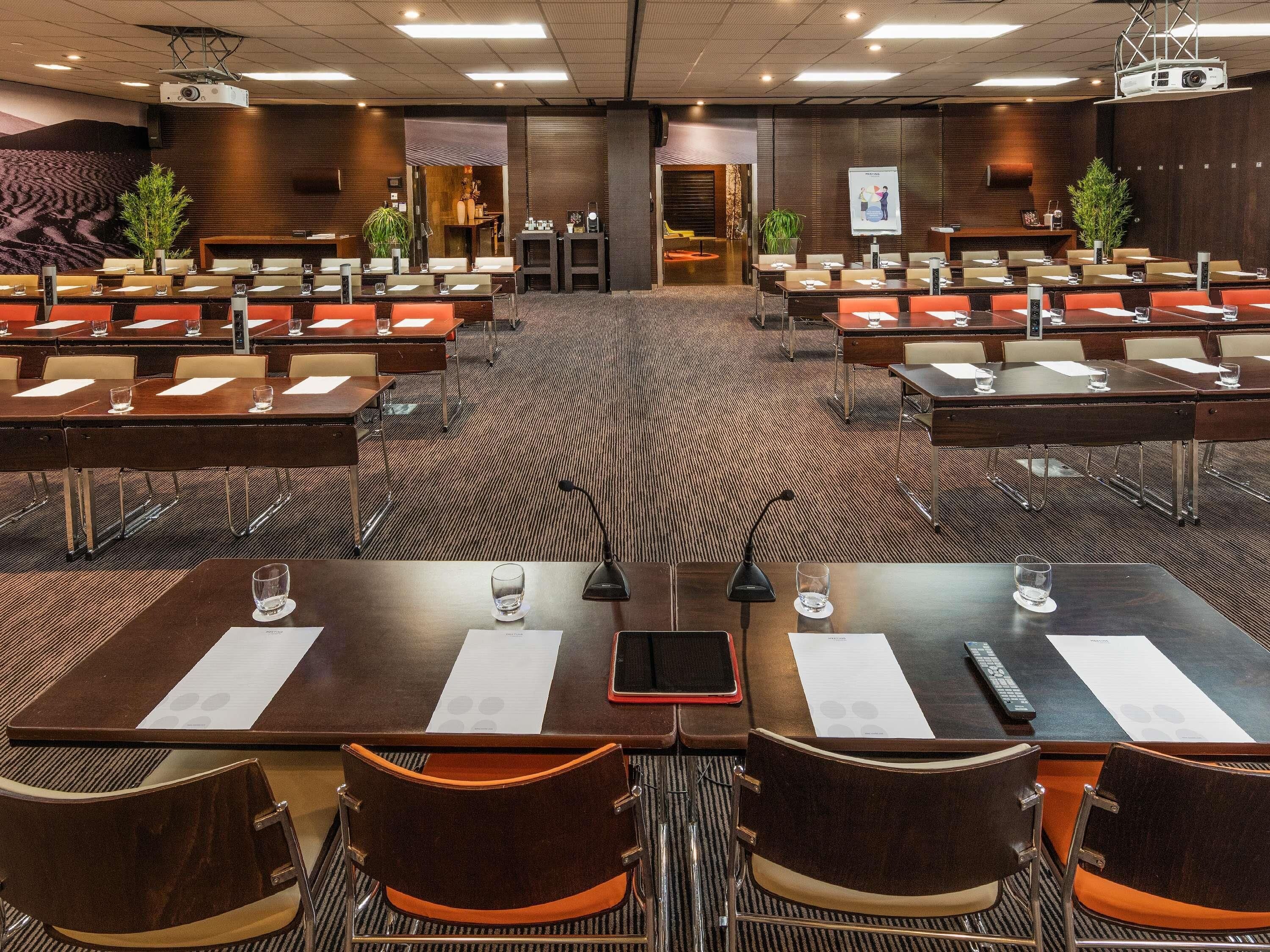 A conference room with multiple tables and chairs, a projector, and a large screen.