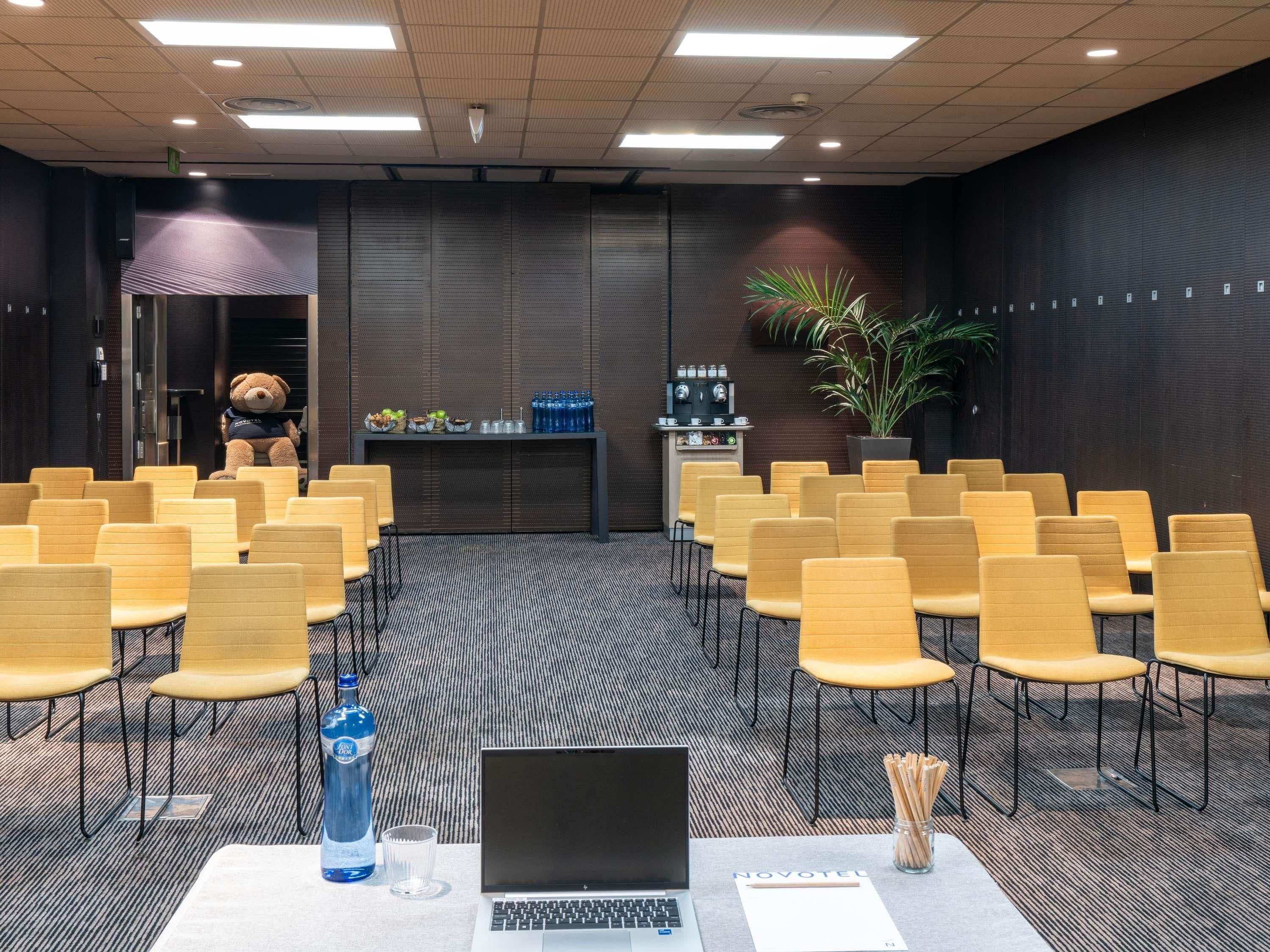 A conference room with rows of yellow chairs, a laptop on a table, a water bottle, and a plant.