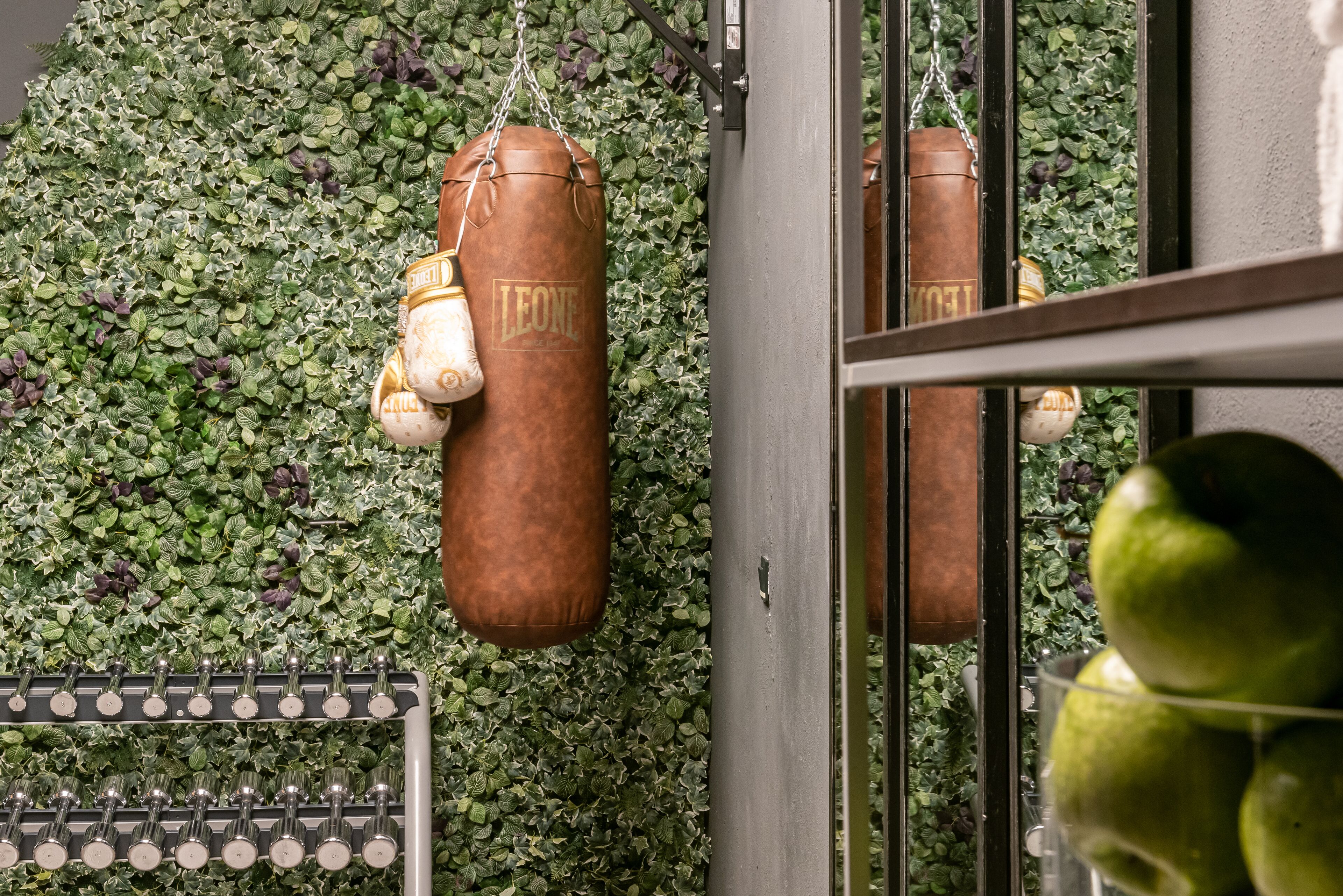 A gym with punching bags and a wall of green foliage.
