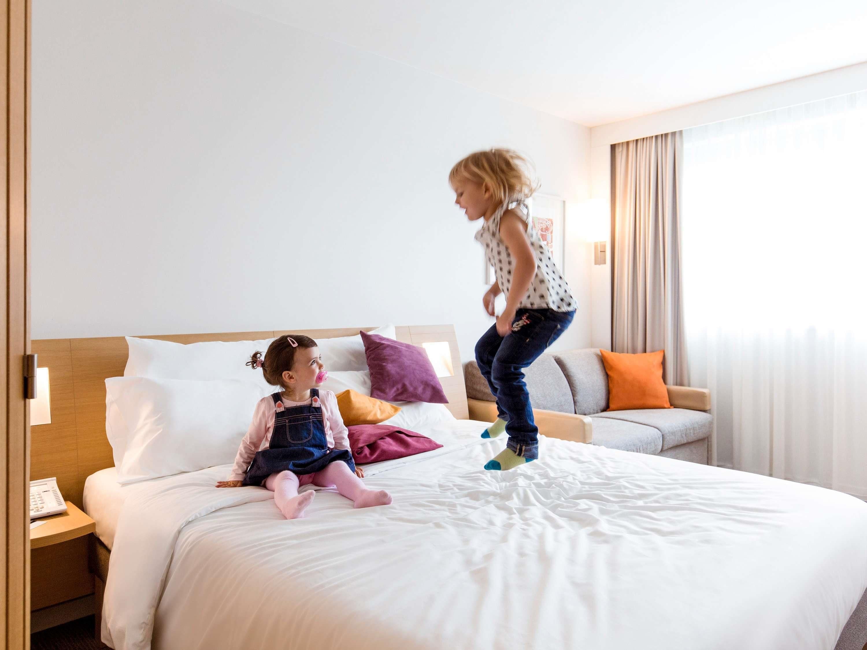 A hotel room with a bed, a nightstand, a sofa, and a window with curtains.