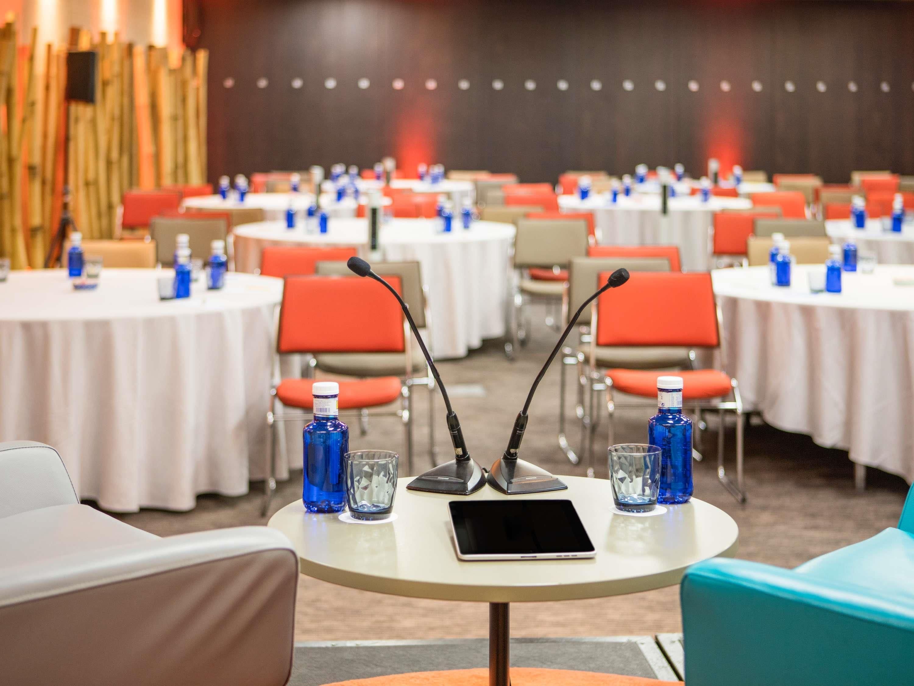 A conference room with round tables, chairs, microphones, and water bottles.