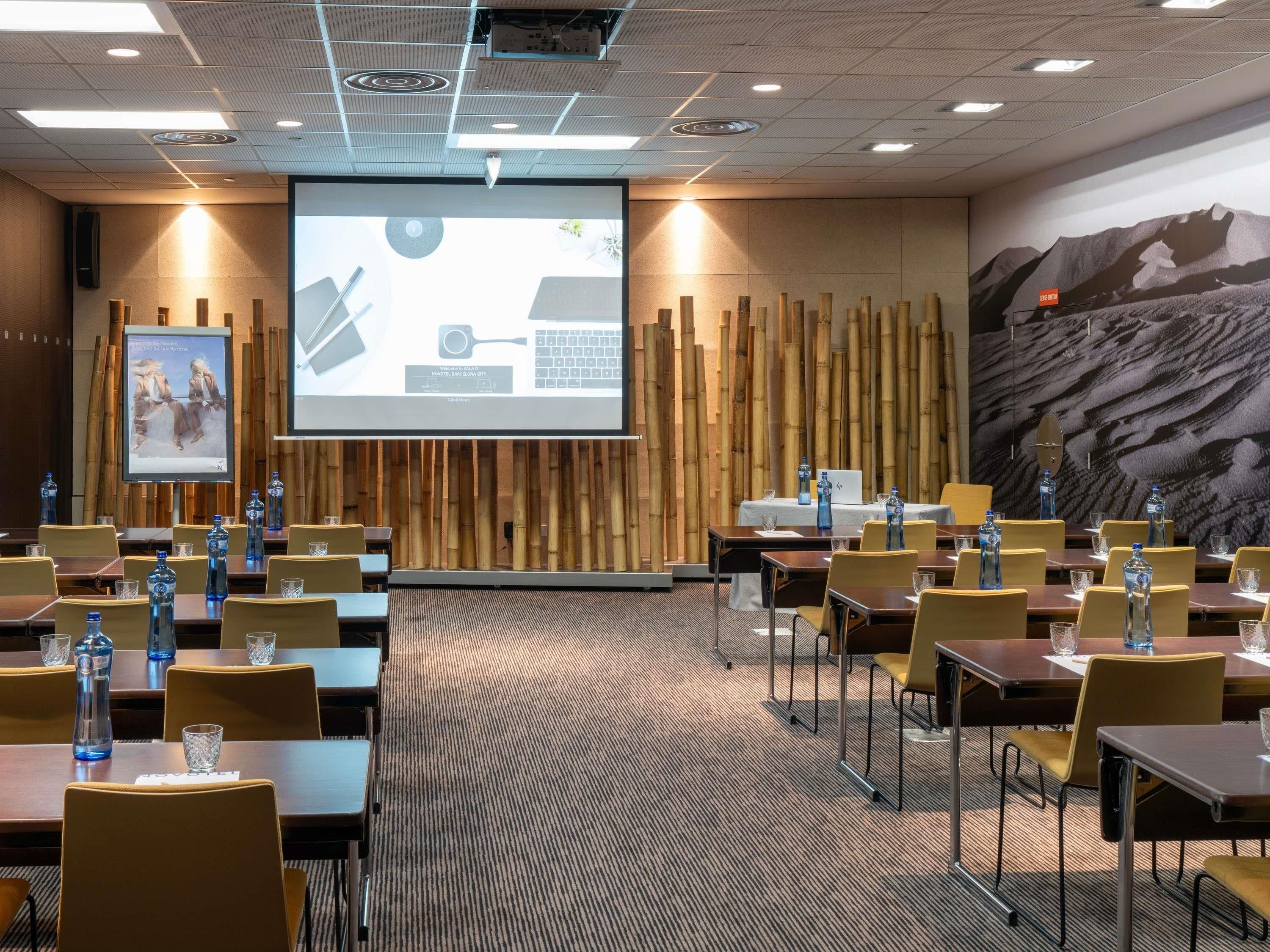 A conference room with tables, chairs, a projector screen, and a large wall mural.