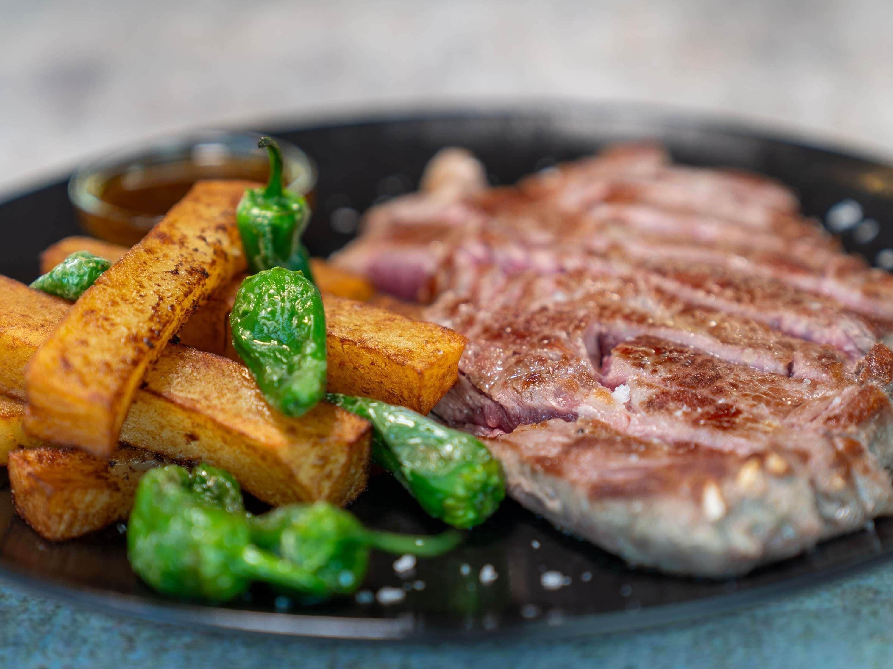 Un plato con bistec a la parrilla, papas asadas y pimientos verdes.