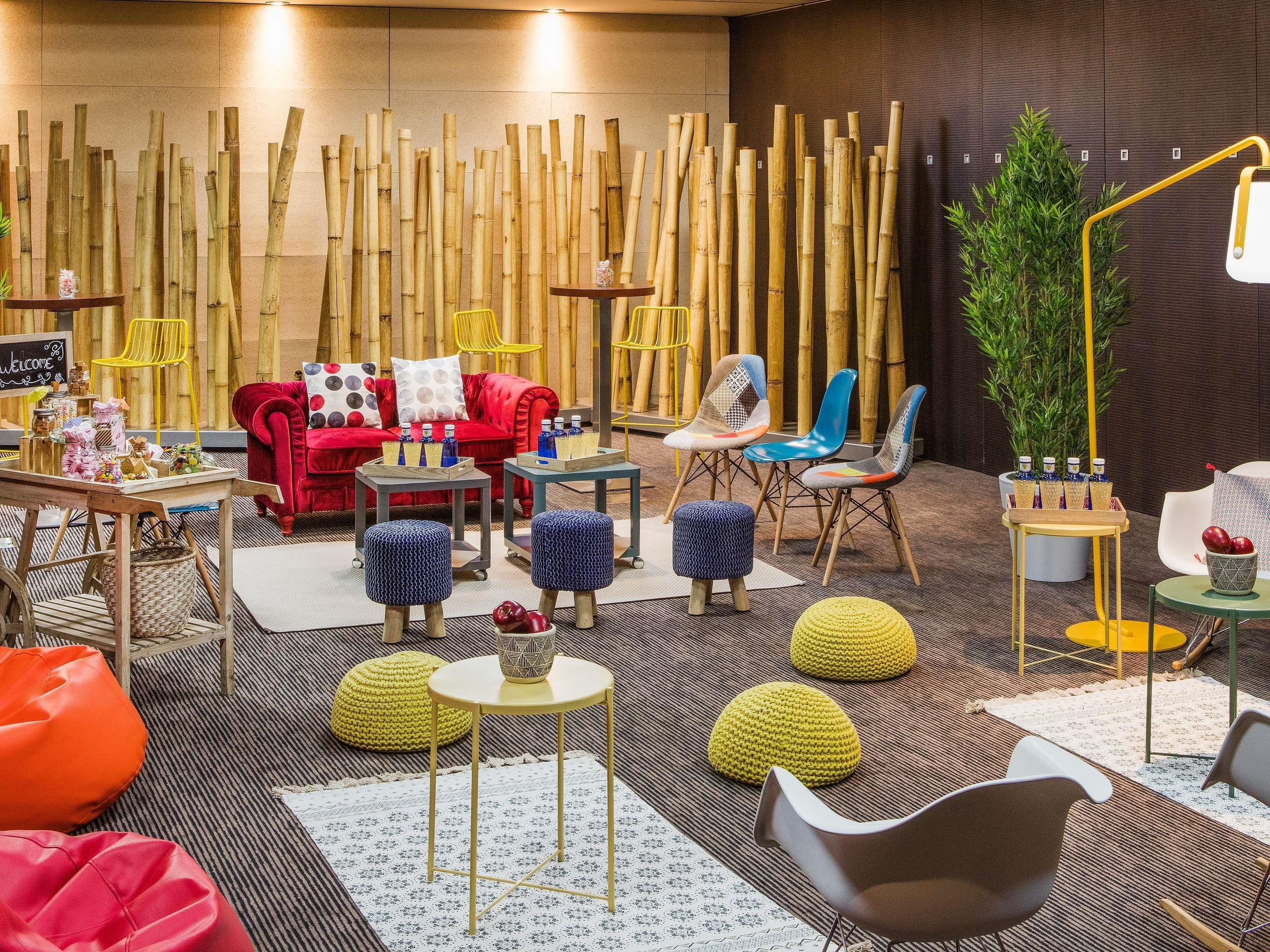 Um interior moderno com decoração em bambu, um sofá vermelho, cadeiras coloridas e uma pequena mesa com garrafas.