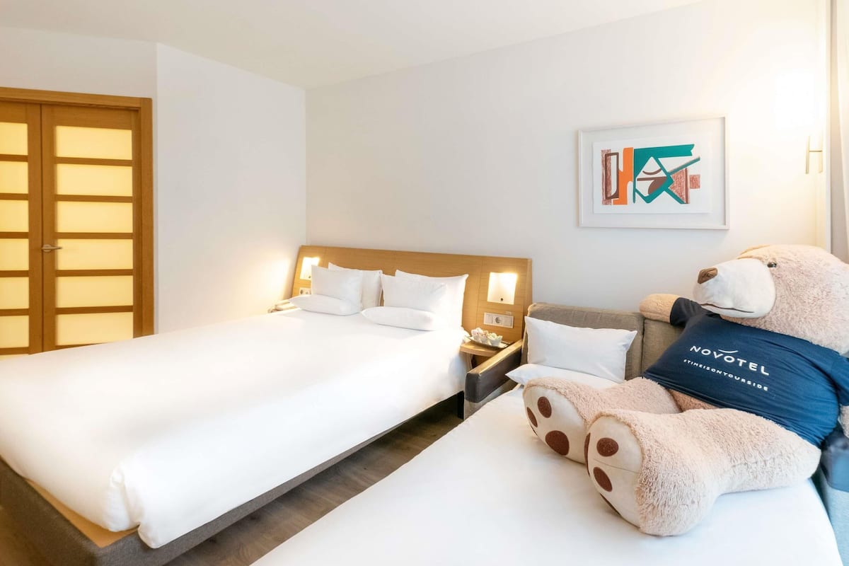 A hotel room with a bed, a nightstand, a teddy bear, and a wooden door.