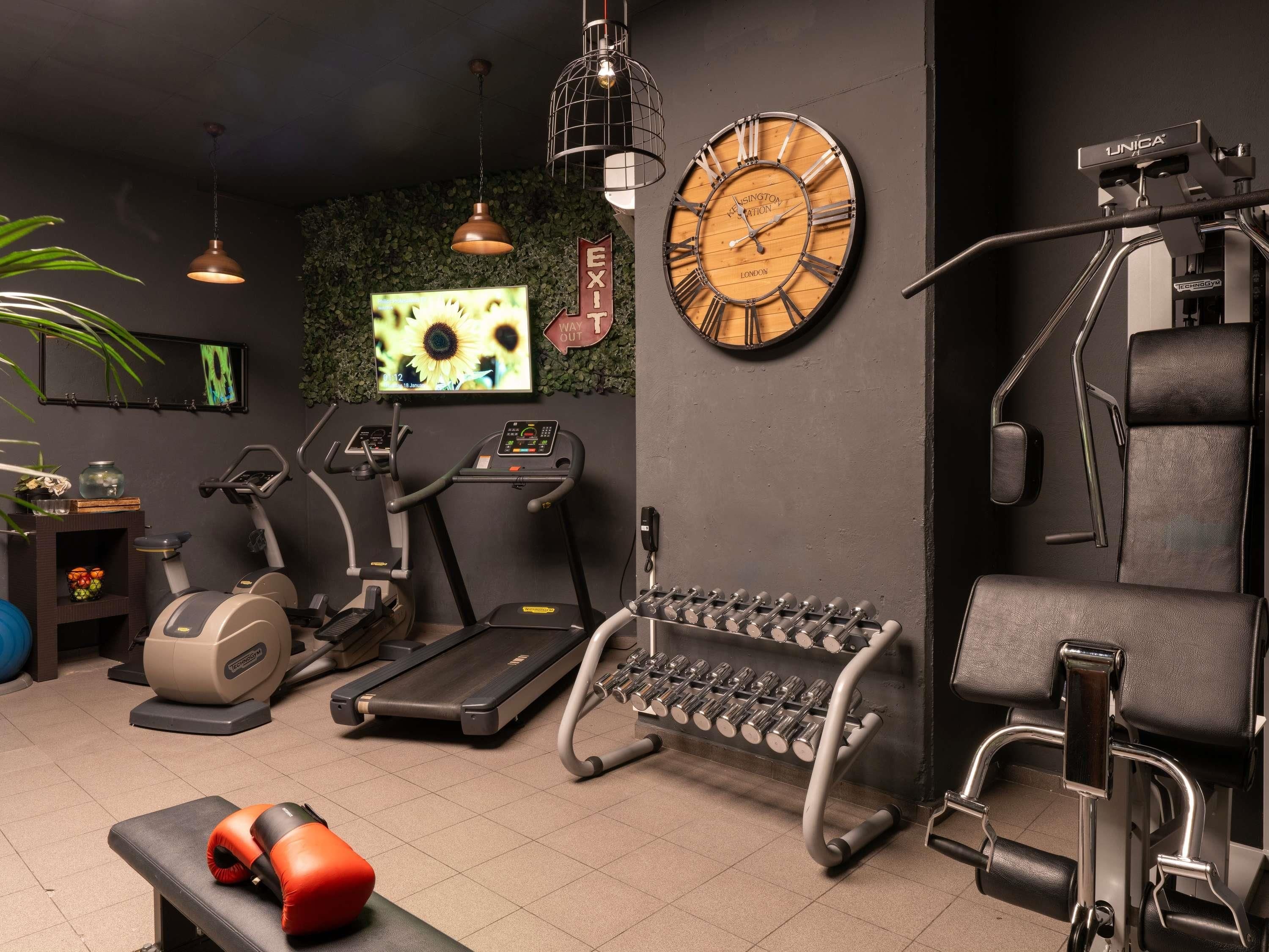 Une salle de sport équipée de matériel d’exercice, avec une horloge murale et un écran de télévision.