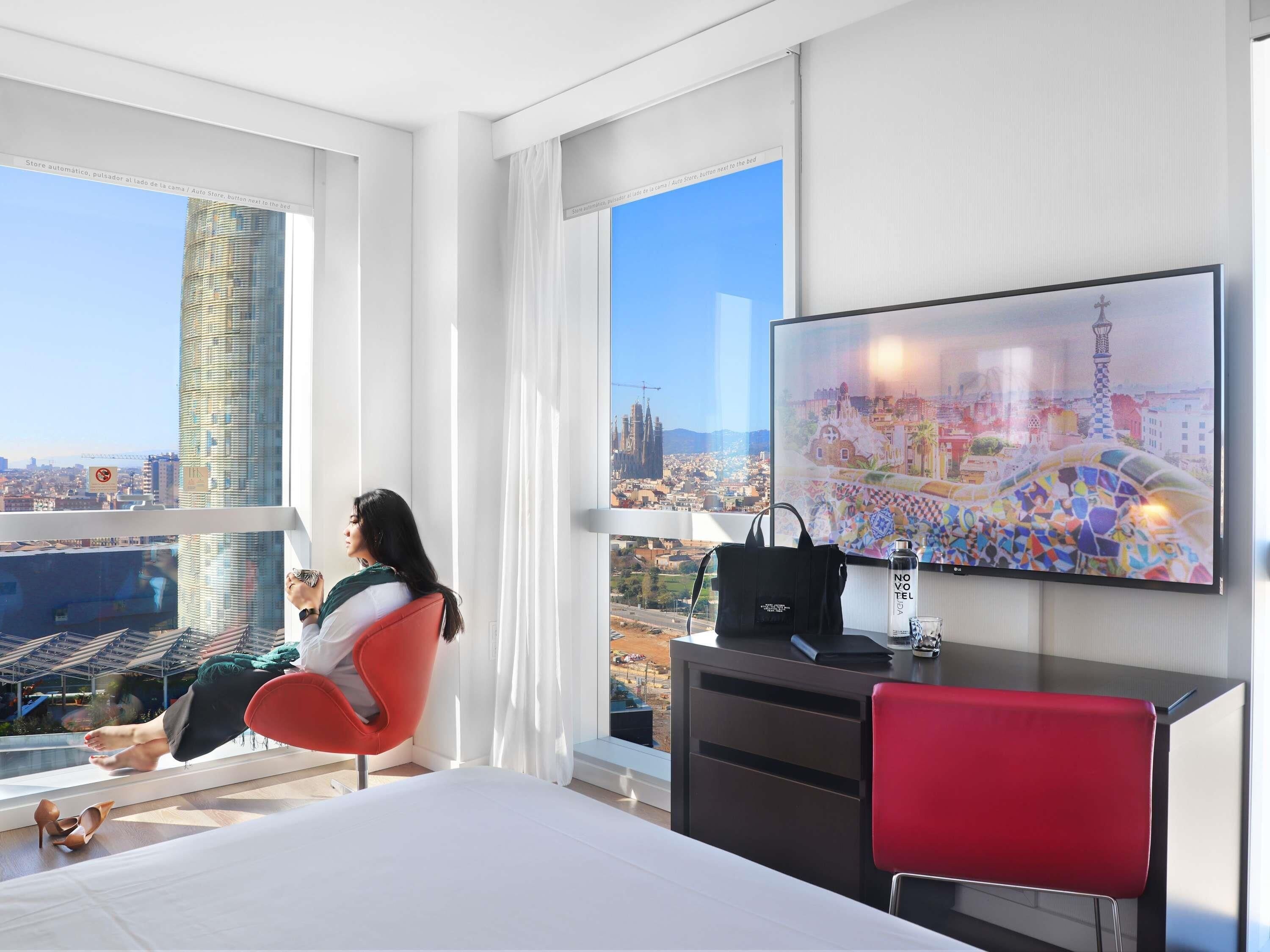 Una habitación de hotel moderna con una cama grande, un escritorio, una silla y un televisor que muestra un paisaje urbano.