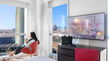 A modern hotel room with a large bed, a desk, a chair, and a TV displaying a cityscape.