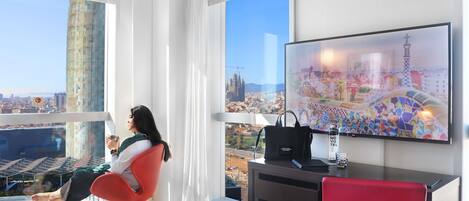 Una habitación de hotel moderna con una cama grande, un escritorio, una silla y un televisor que muestra un paisaje urbano.