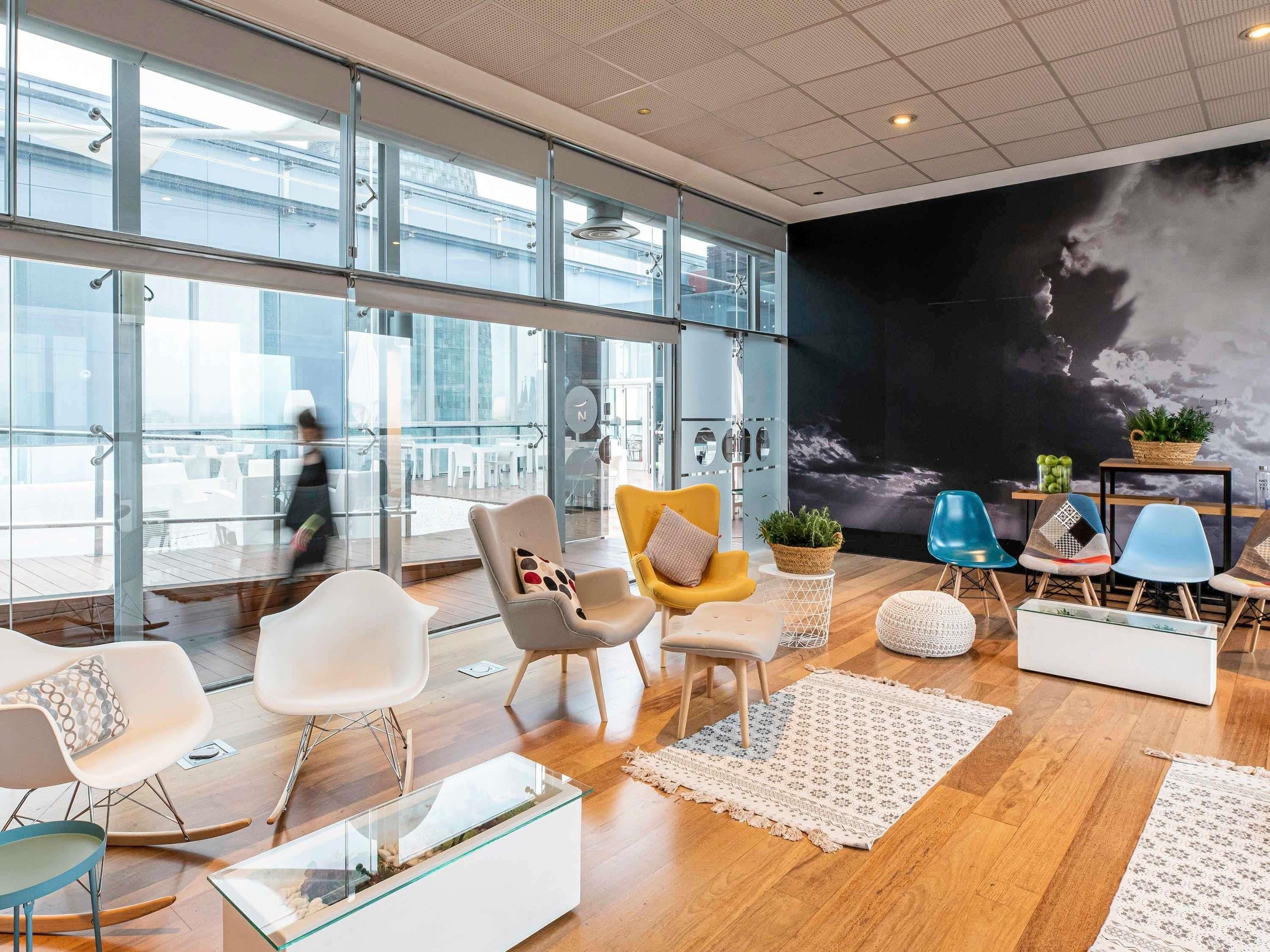 A modern lounge area with glass walls, wooden flooring, and various seating options including chairs and a sofa.